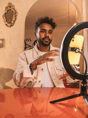 Man in beige jacket using ring light setup for video call indoors.