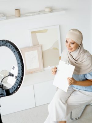 Woman in hijab using ring light indoors for creating lifestyle vlog content.