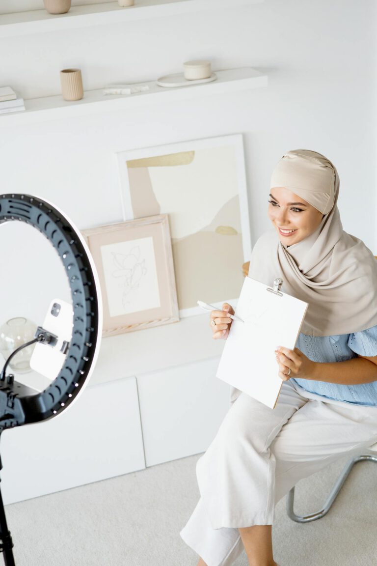 Woman in hijab using ring light indoors for creating lifestyle vlog content.