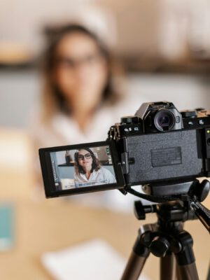 Woman recording video with DSLR camera, displaying on screen.
