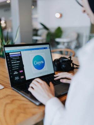 Young woman designing with Canva on laptop in a stylish indoor setting, accompanied by a digital camera.